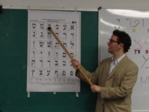 Hebrew Teacher standing before whiteboard with Hebrew alphabet